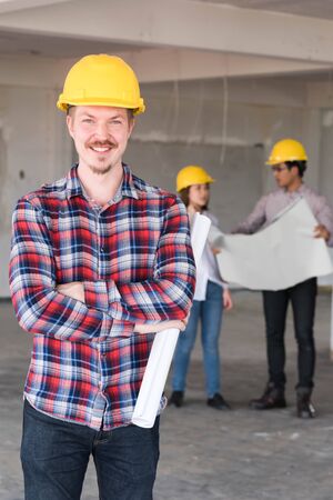 Construction engineer smile wear yellow safety helmet with blue print of construction plan in handの写真素材