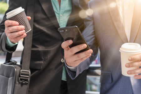 Two Westerner Business men talk and use smartphone with paper cup of hot coffee in handsの写真素材