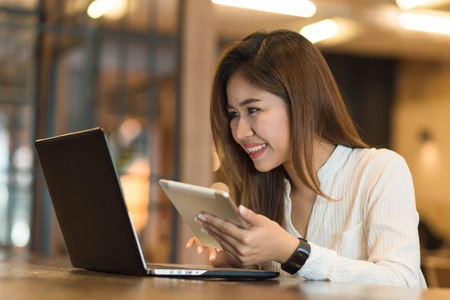 Woman holding tablet  while using laptop, freelance or nadmad worker conceptualの写真素材