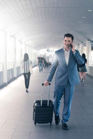 Business man with travel bag use smart phone on the walk way with crowded people in backgroundの写真素材