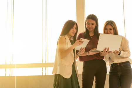 Three woman use laptop together in afternoon sunの写真素材