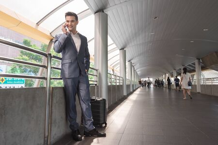 Business man with travel bag use smart phone on the walk way with crowded people in backgroundの写真素材