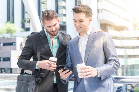 Two Westerner Business men talk and use smartphone with paper cup of hot coffee in handsの写真素材