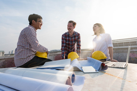 three construction engineers finished working outdoors in construction site with blueprint on tableの写真素材