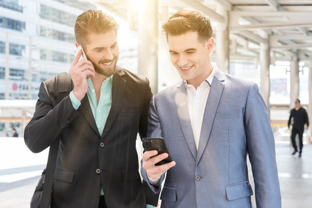 Two Westerner Business men talk and use smart phoneの写真素材