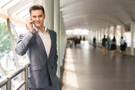 Business man talking via smart phone on the walk way with people in backgroundの写真素材