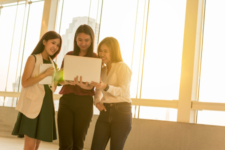 Three woman use laptop together in afternoon sunの写真素材