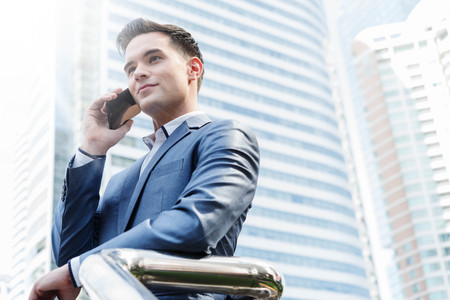 Westerner Business man talking via smart phone with skyscraper in backgroundの写真素材