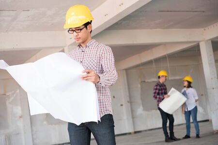 Close up asian Construction engineer wear yellow safety helmet with blue print of construction plan in handの写真素材