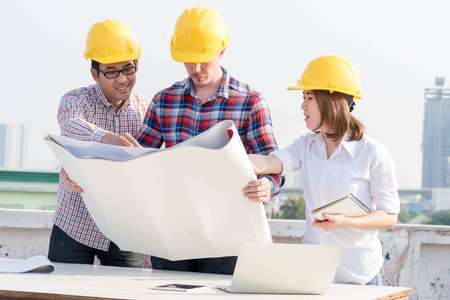 three construction engineers working outdoors in construction site with blueprint on tableの写真素材