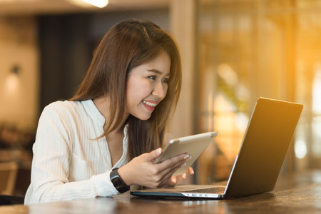 Woman holding tablet  while using laptop, freelance or nadmad worker conceptualの写真素材