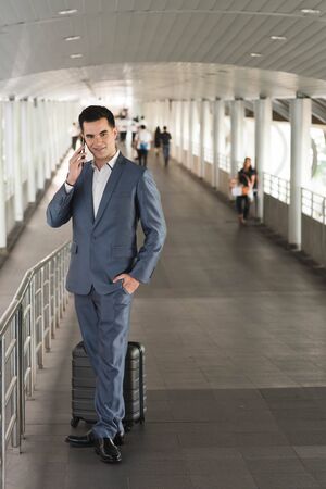 Business man traveling use smart phone on the walk way with crowded people in backgroundの写真素材