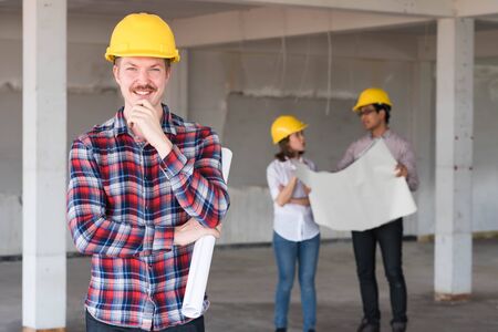 Westerner Construction engineer smile wear yellow safety helmet with blue print of construction plan in handの写真素材