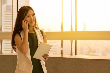 Pretty woman talk via cell phone and hold a tabletの写真素材