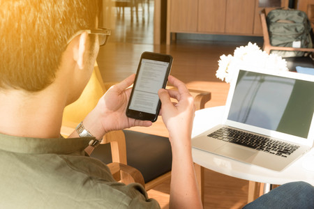 Young man use smartphone and laptop in afternoon, technology lifestyle of new generation of nomad workersの写真素材