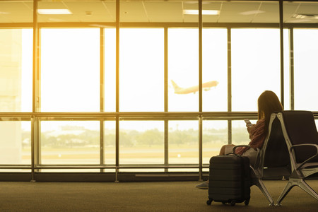 Young beautiful woman in airport with travel bag use smartphone at airport wait for flight, world exploration conceptの写真素材
