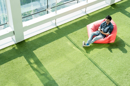 Man use smartphone on bean bag in afternoon, freelance conceptual lifestyle, internet in everyday lifeの写真素材