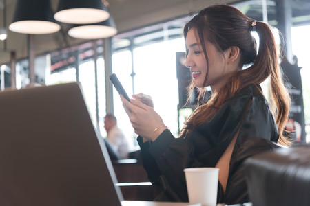 Beautiful asian woman in black dress working with laptop and smartphone in coffeeshopの写真素材