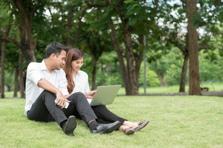 Businessman and woman use laptop in park, sit on grass togetherの写真素材