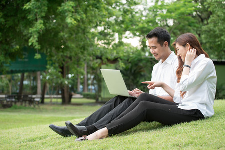 Businessman and woman use laptop in park, sit on grass togetherの写真素材