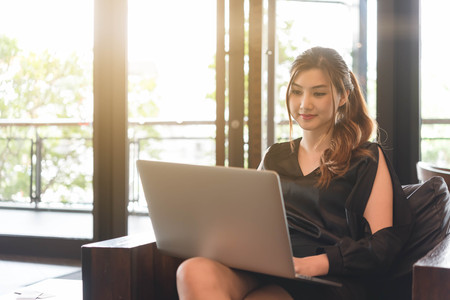 Beautiful asian woman in black dress working with laptop in coffeeshopの写真素材