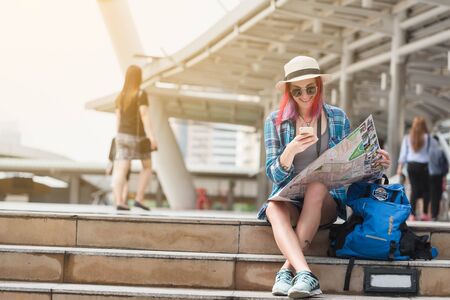 Woman westerner looking at map and smartphone during city tour in the morning, planning for today's tripの写真素材
