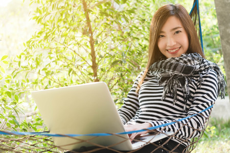 Young woman with scarf use laptop lying in hammock, freelance life style conceptual, work anywhereの写真素材