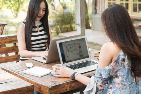 Two Woman us laptop and smartphone in coffee shop with blank screen for template editableの写真素材