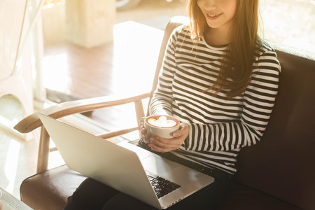 Beautiful young teenage woman freelance work with laptop have coffee at coffee shop in with sun light, freelance lifestyle conceptual, life of coffee loverの写真素材
