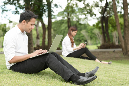 Man on white shirt use laptop in green part with woman use smartphone in backgroundの写真素材