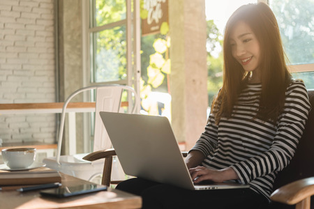 Beautiful young teenage woman freelance work with laptop at coffee shop in with sun light, freelance lifestyle conceptualの写真素材