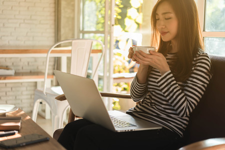 Beautiful young teenage woman freelance work with laptop have coffee at coffee shop in with sun light, freelance lifestyle conceptual, life of coffee loverの写真素材