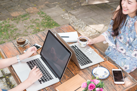 Two teenage women meet in coffee shop use laptop together in afternoon, life style of new teenager with blank screen on laptopの写真素材