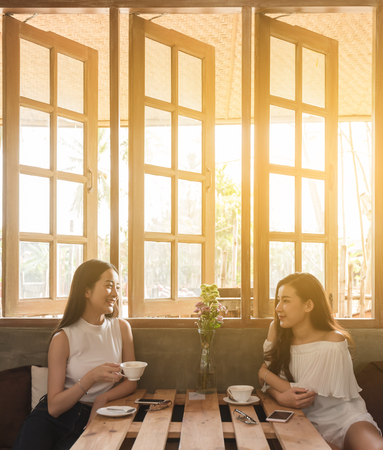 Two teenage women meet in coffee shop use smartphone play social media together in afternoon, life style of new teenagerの写真素材