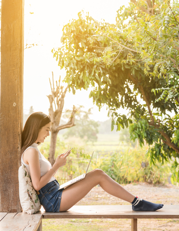 Beautiful asian woman teenager use laptop and smartphone with sun lightの写真素材