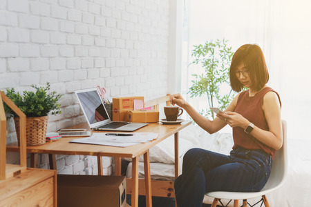 Woman small business owner, business start up conceptual, young entrepreneur use internet with smartphone during morning coffeeの写真素材