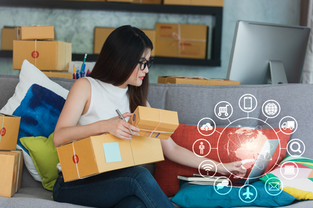 Young asian woman use smartphone and laptop run own business at home, internet of things conceptual, young entrepreneur with technologyの写真素材