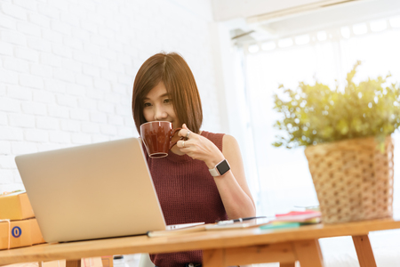 Woman small business owner, business start up conceptual, young entrepreneur check on laptop in the morning with coffee cupの写真素材
