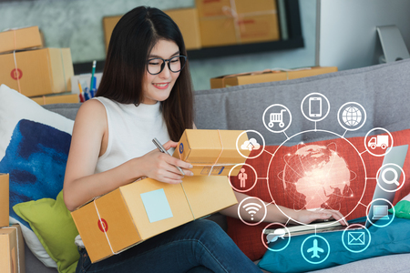 Young asian woman use smartphone and laptop run own business at home, internet of things conceptual, young entrepreneur with technologyの写真素材