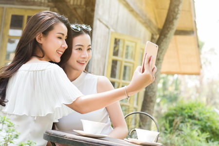Life of generation Y teenagers hang out in coffee shop use smartphone play social media sharing digital content to each other with fun take selfie shotの写真素材