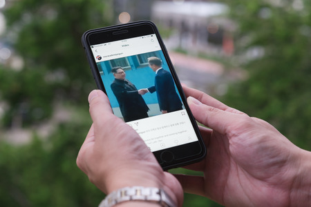 BANGKOK, THAILAND- 30th April 2018 :Hands of woman with joy watching video clip of Kim Jong-un, north korean leader shaking hands with Moon Jae-in, president of south korea via Instagram applicationのeditorial素材