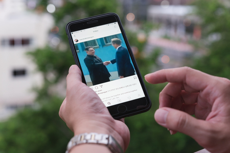 BANGKOK, THAILAND- 30th April 2018 :Hands of woman with joy watching video clip of Kim Jong-un, north korean leader shaking hands with Moon Jae-in, president of south korea via Instagram applicationのeditorial素材
