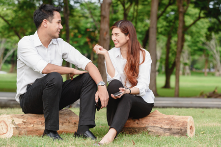 Man and woman in white shirt talk to each other in outdoors parkの写真素材