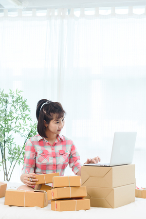 Woman small business owner, business start up in bedroom, young entrepreneur work with laptop prepare parcel boxes for deliver to customerの写真素材