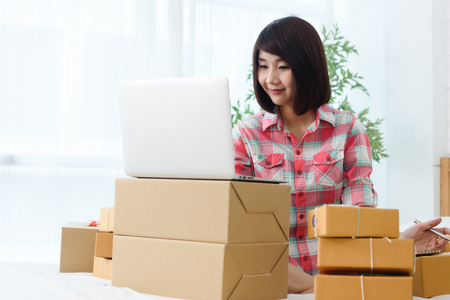 Woman small business owner, business start up in bedroom, young entrepreneur work with laptop prepare parcel boxes for deliver to customerの写真素材