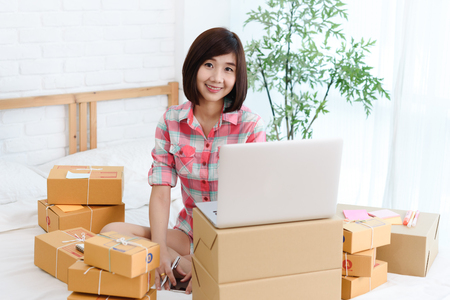 Woman small business owner, business start up in bedroom, young entrepreneur work with laptop prepare parcel boxes for deliver to customerの写真素材
