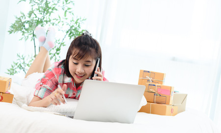Woman small business owner, business start up in bedroom, young entrepreneur work with laptop prepare parcel boxes for deliver to customerの写真素材