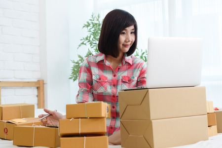 Woman small business owner, business start up in bedroom, young entrepreneur work with laptop prepare parcel boxes for deliver to customerの写真素材