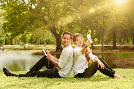 Man and woman in white shirt use smartphone together in outdoors park take selfie shotの写真素材
