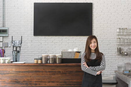 Young woman owner of a cafe stand in front of coffee counter, young entrepreneur conceptual, blank black board on wallの写真素材